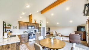 A spacious kitchen with wooden cabinets, a dining area with a round table and chairs, and a living area with a sofa and television. - Balcony & Patio w/ Mtn Views! Bonners Ferry Escape (Bonners Ferry)