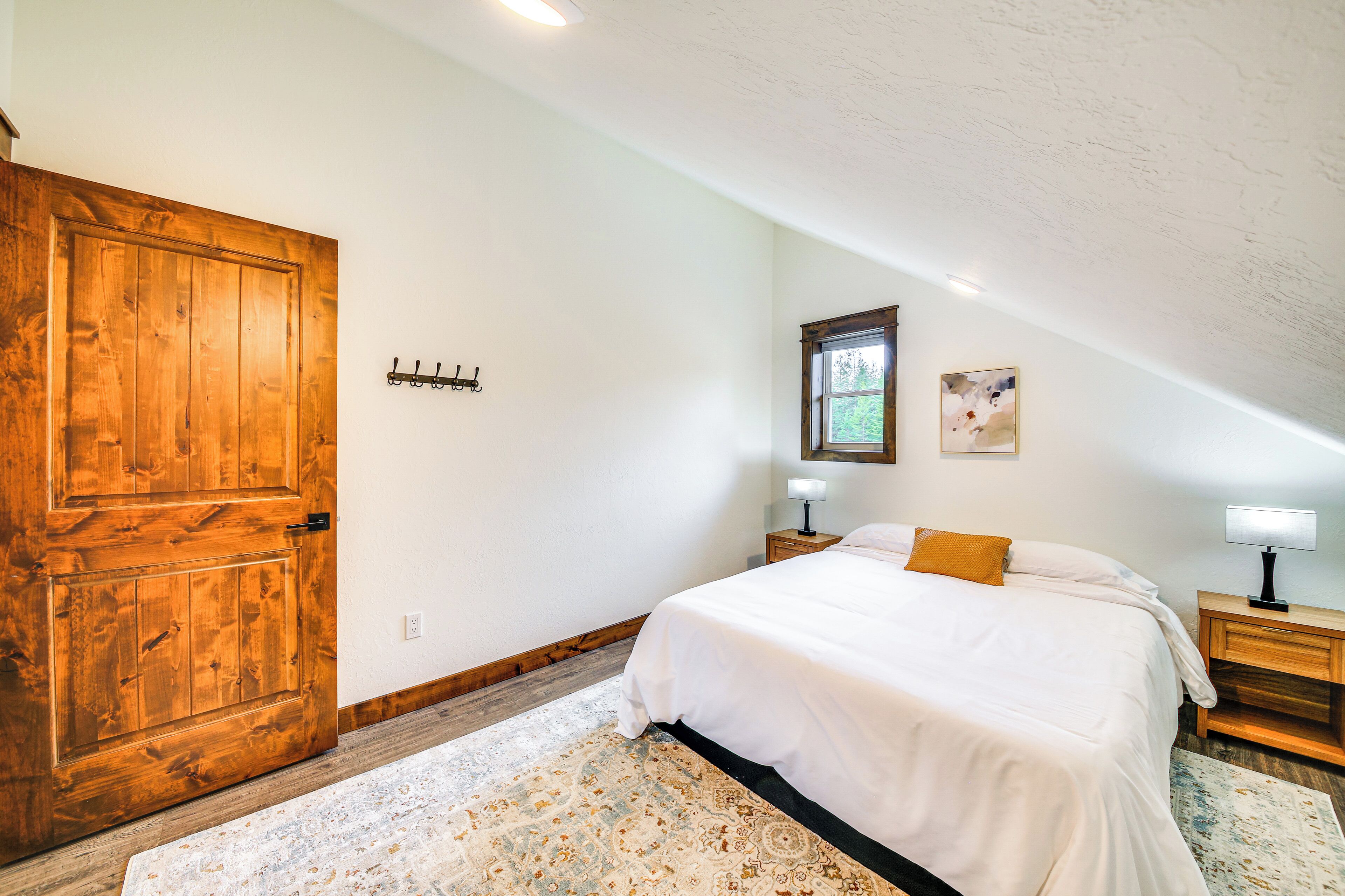 A bedroom with a large wooden door, a bed with white bedding, two bedside tables with lamps, and a patterned rug.
