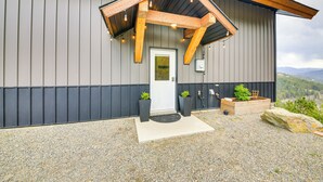 A modern building with a sloped roof, a wooden porch, and a gravel driveway. - Balcony & Patio w/ Mtn Views! Bonners Ferry Escape (Bonners Ferry)