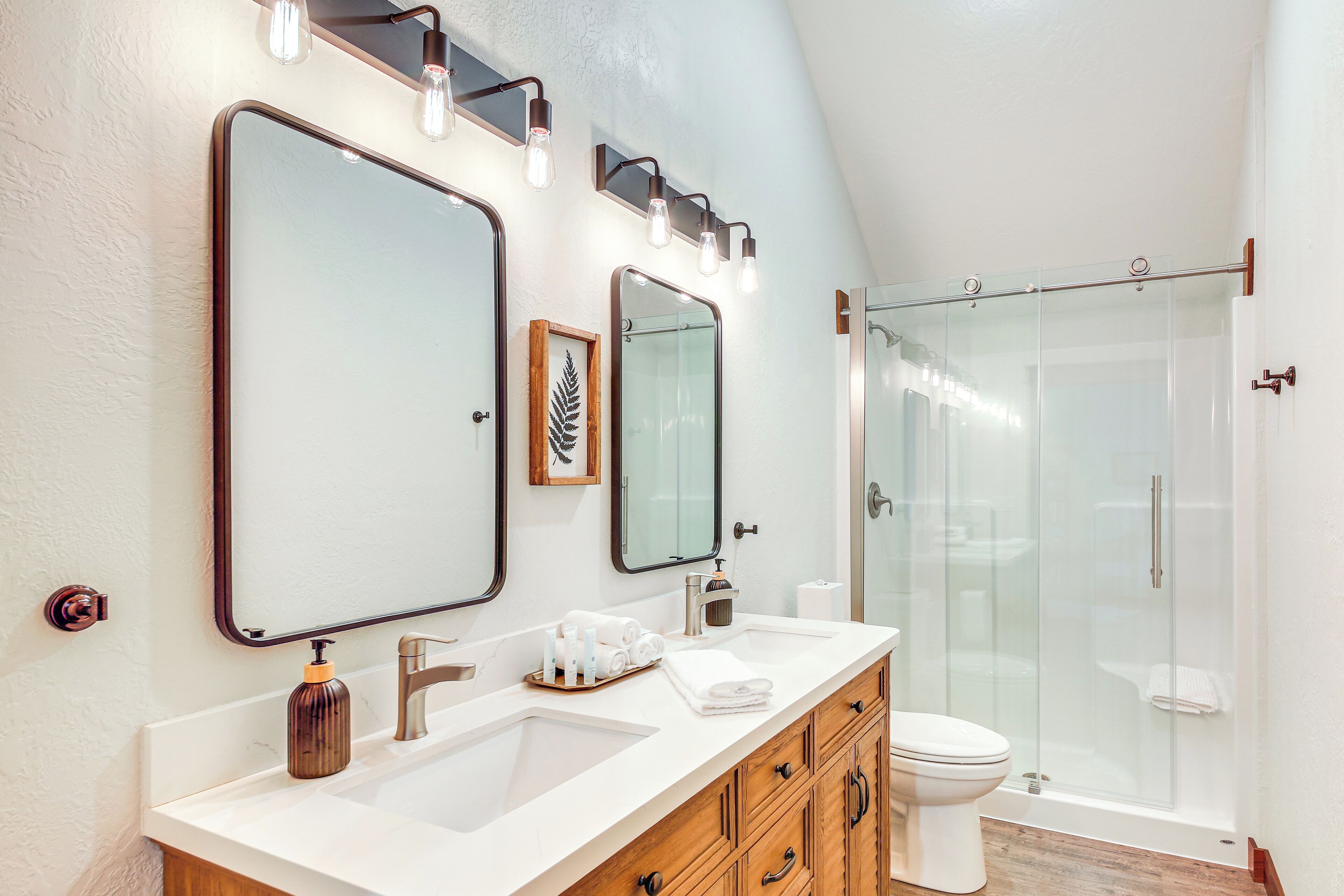 Une salle de bain moderne avec un grand miroir, deux lavabos, des toilettes et une douche à parois de verre.