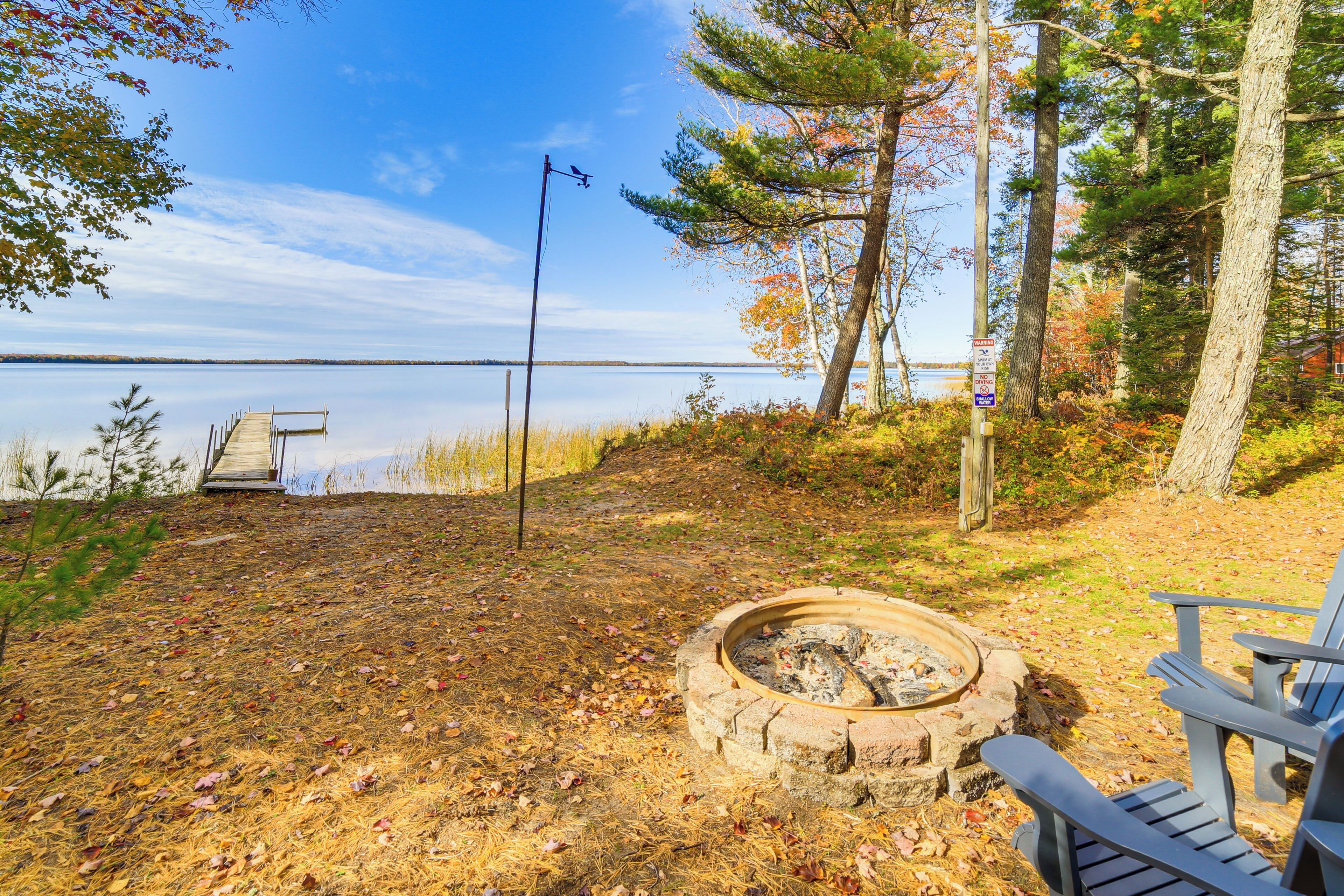 A lakeside campsite with a fire pit, a dock, and a chair.