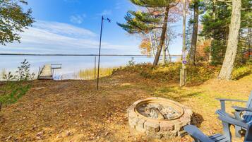 A lakeside campsite with a fire pit, a dock, and a chair.