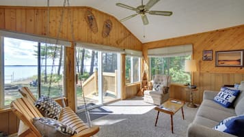 Ein geräumiges Zimmer mit großem Fenster und Blick auf ein Gewässer, einem Deckenventilator und einer gemütlichen Sitzecke mit Sofa und Sesseln.