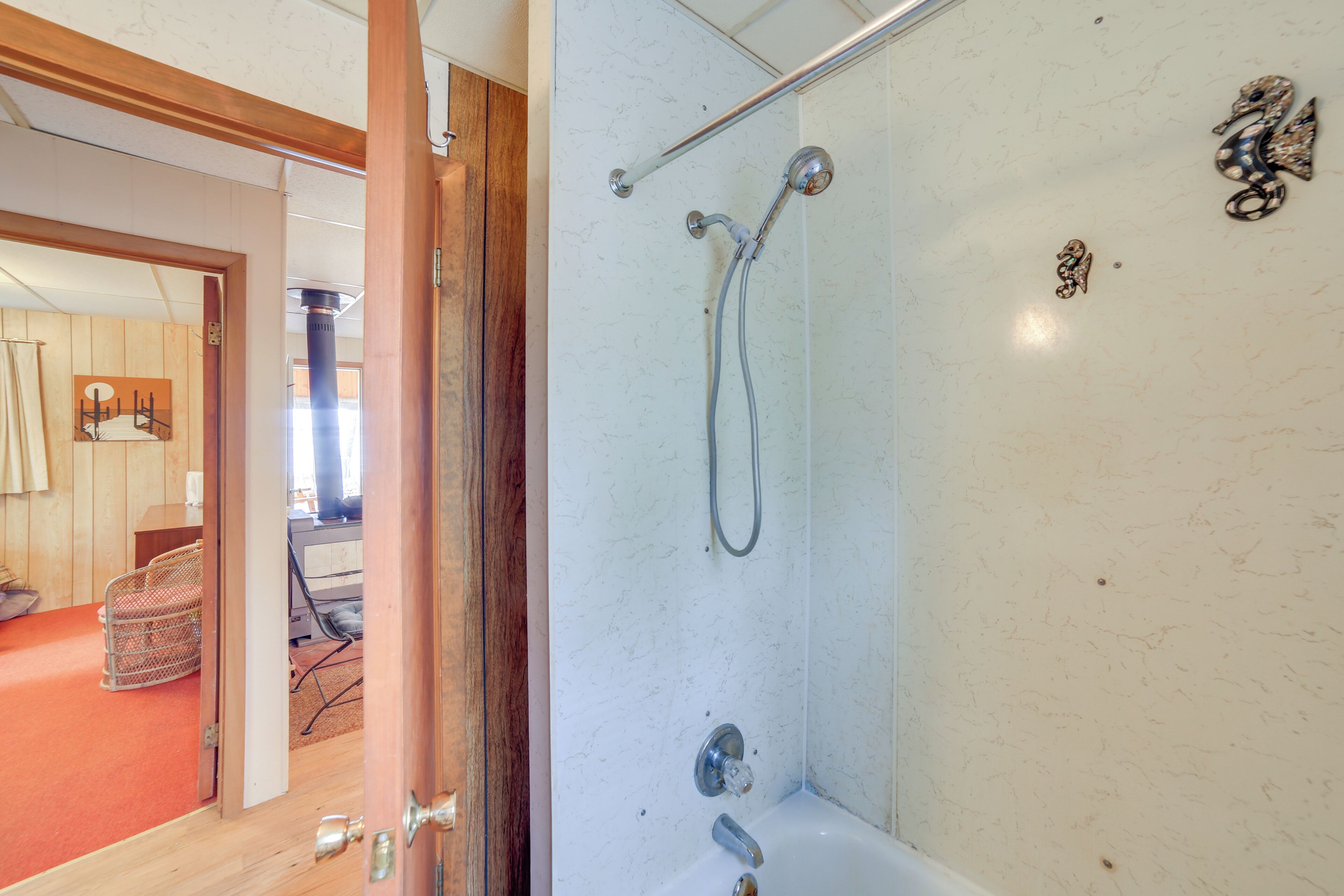 A bathroom with a shower, a toilet, and a sink. There is a wooden door leading to another room.