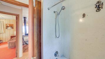 A bathroom with a shower, a toilet, and a sink. There is a wooden door leading to another room.