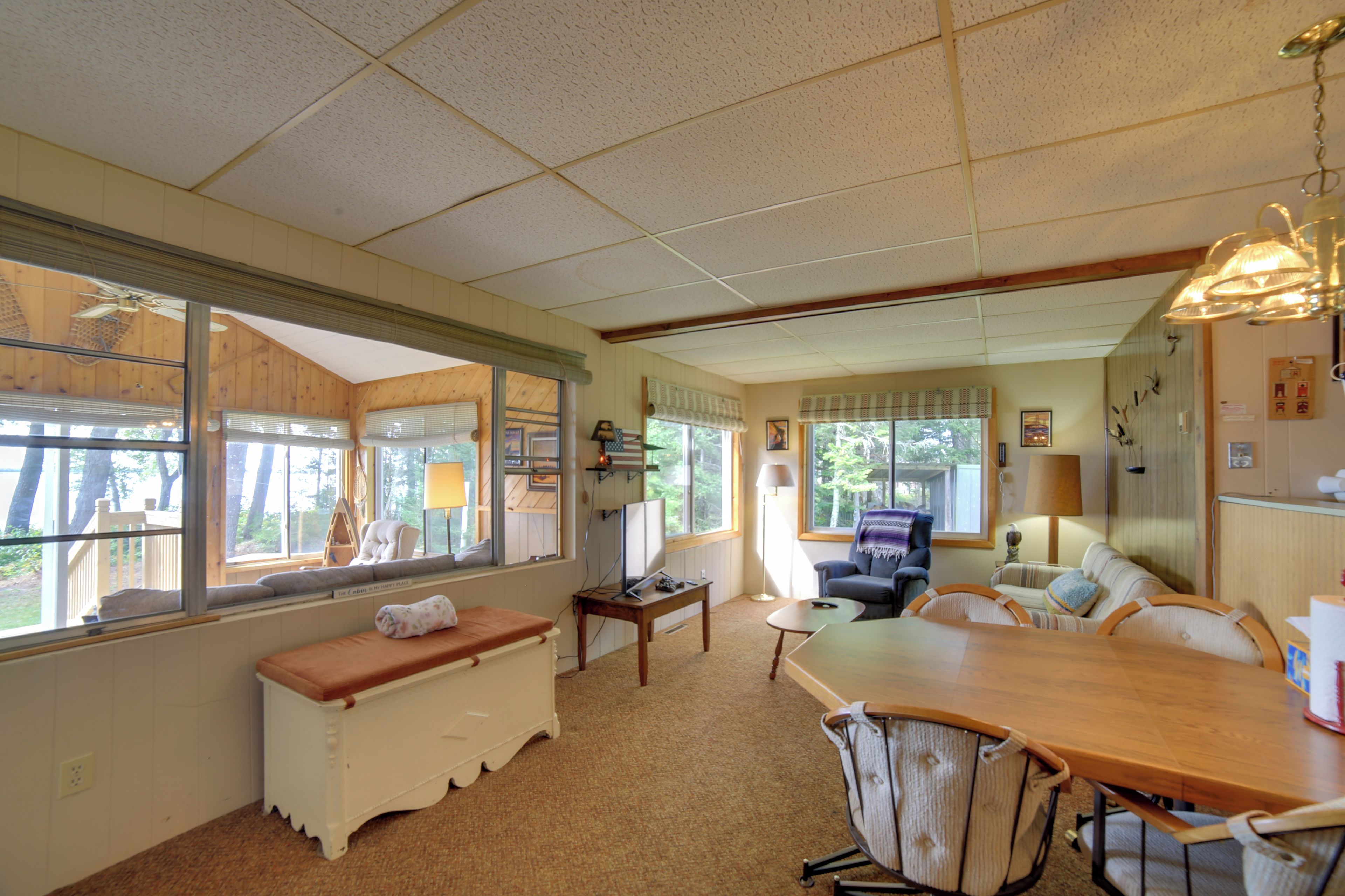 A spacious living area with a large wooden dining table, comfortable seating, and large windows offering views of the outdoors.