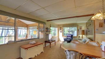 A spacious living area with a large wooden dining table, comfortable seating, and large windows offering views of the outdoors.