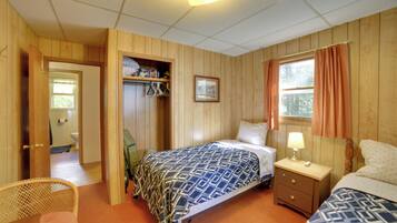 A room with wooden walls, a bed with patterned bedding, a bedside table with a lamp, and a window with curtains.