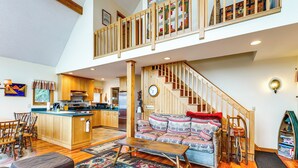 A spacious living area with a wooden staircase, a sofa, a dining table, and a kitchen in the background. - 'sweet Serenity' Schroon Lake Family Retreat! (Schroon Lake)