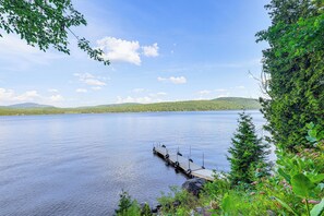 A calm lake with a wooden dock extending into the water, surrounded by lush greenery and distant hills. - 'sweet Serenity' Schroon Lake Family Retreat! (Schroon Lake)