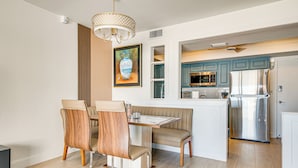 A modern kitchen with a stainless steel refrigerator, a microwave, and a sink. There is a dining area with a wooden table and chairs. - Steps to Ocean: Satellite Beach Condo w/ Balcony (Satellite Beach)