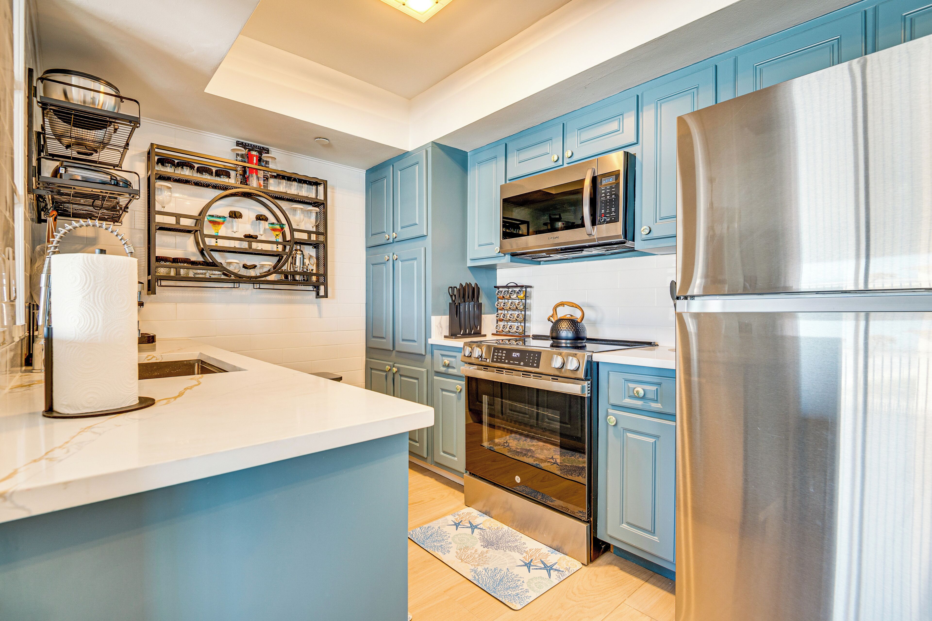 A kitchen with blue cabinets, stainless steel appliances, and a marble countertop.