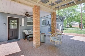 A covered porch with a brick column, a hanging chair, a welcome sign, and a door with a floral wreath.
