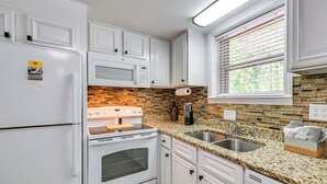 Una cocina con gabinetes blancos, encimera de granito, pileta de acero inoxidable y protector contra salpicaduras de ladrillo.
