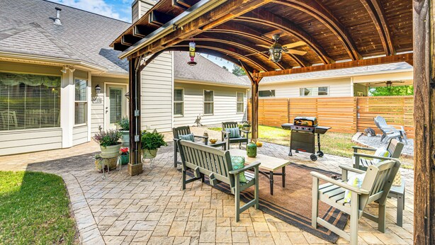 Un patio cubierto con mobiliario exterior, una parrilla y una valla de madera.