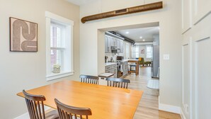 Zona pranzo con tavolo e sedie in legno, una cucina sullo sfondo e una grande bocchetta d'aria sul soffitto.