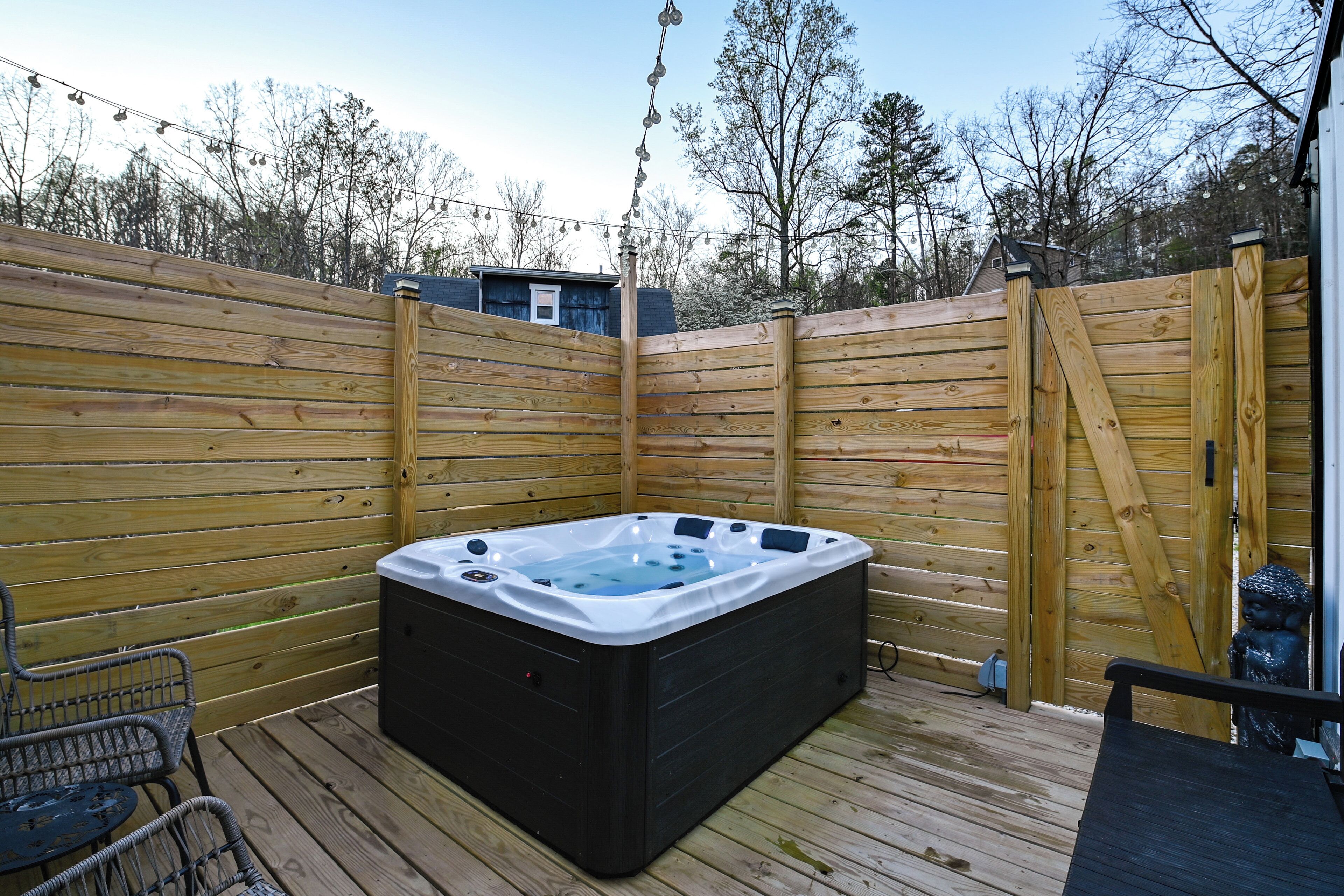 A hot tub on a wooden deck with a fence, a Buddha statue, and a small table.