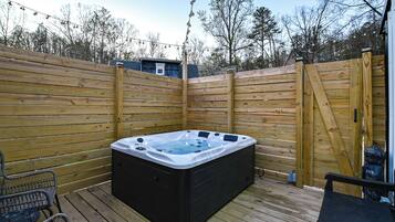A hot tub on a wooden deck with a fence, a Buddha statue, and a small table.