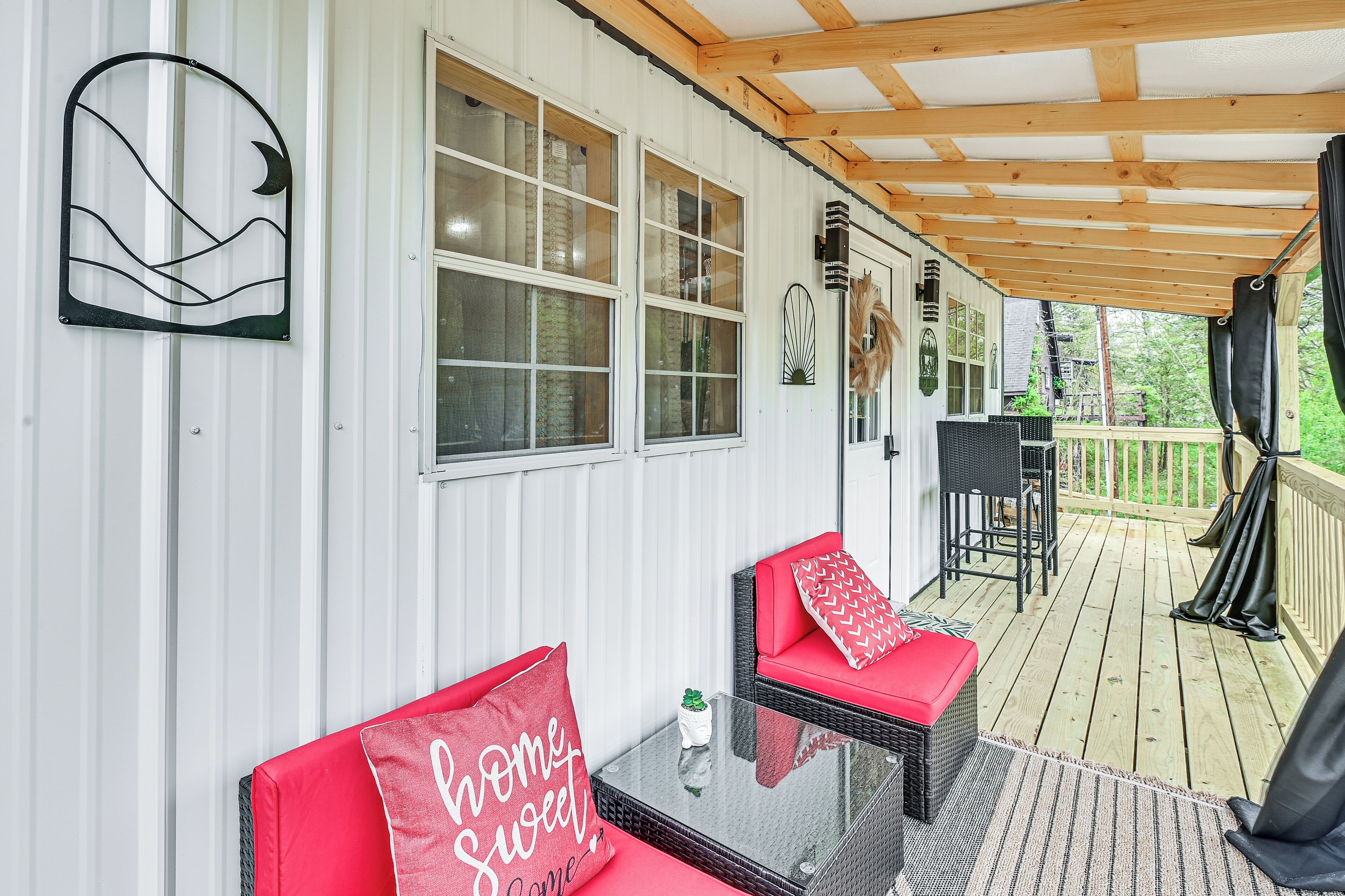 A covered porch with wicker furniture, a glass table, and a red cushion with "Home Sweet Home" text.
