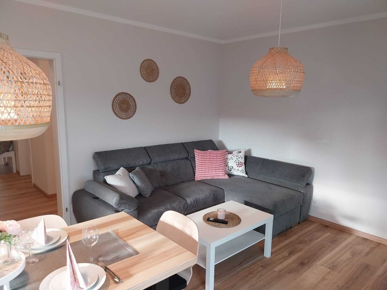 Ein modernes Wohnzimmer mit einem grauen Sofa, einem weißen Couchtisch und einem Essbereich mit einem Holztisch, gedeckt für zwei Personen.