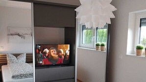 Une chambre moderne avec un lit, une télévision et une fenêtre agrémentée de plantes.