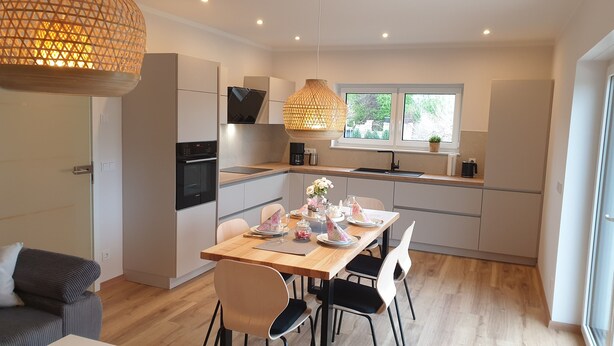 Une cuisine moderne avec un coin repas, comprenant une table en bois, des chaises et des luminaires suspendus.