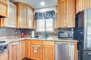 A kitchen with wooden cabinets, a stainless steel refrigerator, a microwave, a dishwasher, a gas stove, and a window with blinds. - 'will's Place' Utah Family Getaway: Hot Tub & Yard (Glendale)