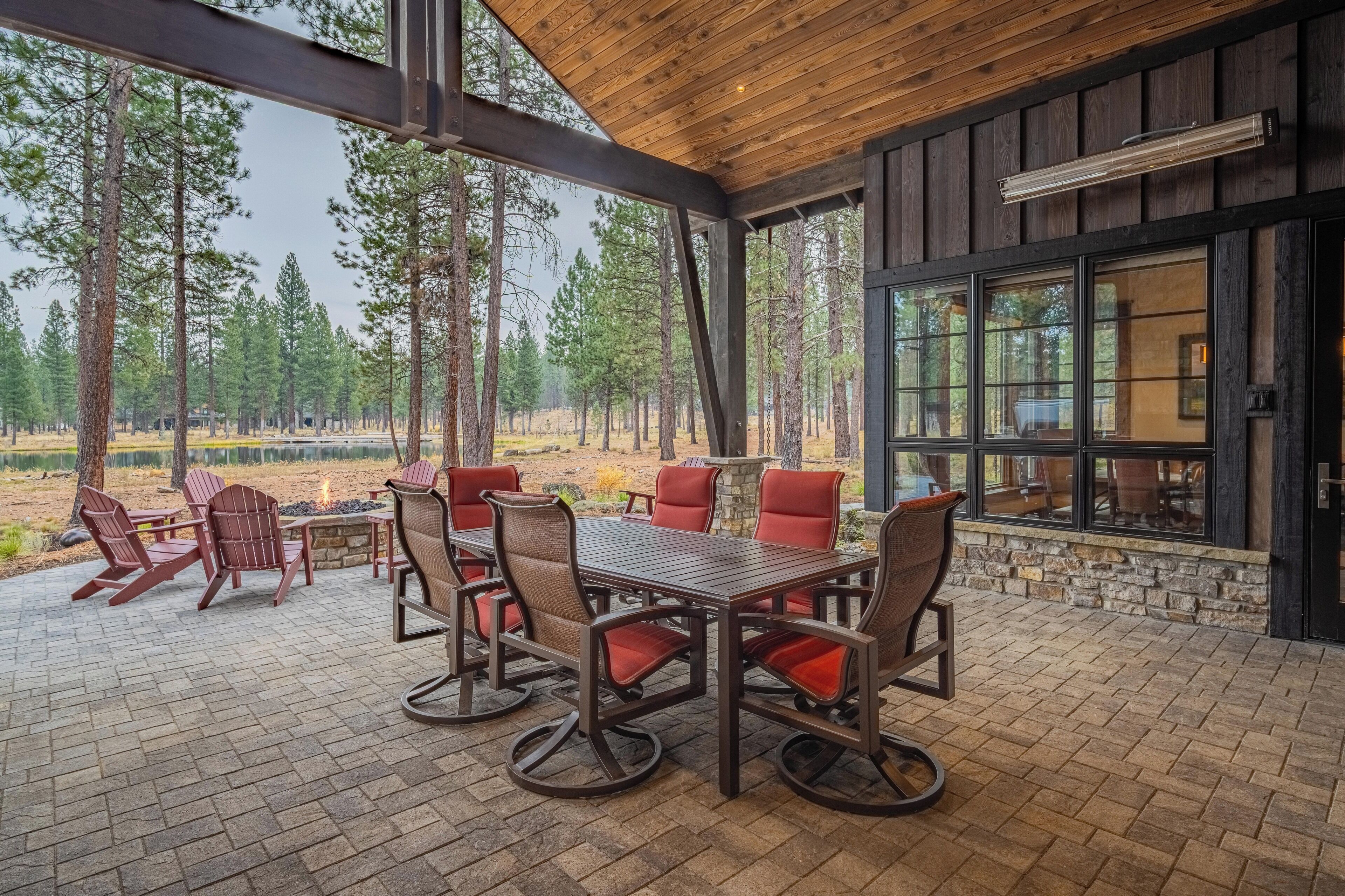 Eine überdachte Terrasse mit Holztisch und -stühlen, umgeben von Steinmauern und großen Fenstern.