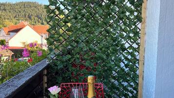 Ein Tisch mit einer Champagnerflasche, einem Glas und einem Blumenstrauß auf einem Balkon mit Gitterwand.