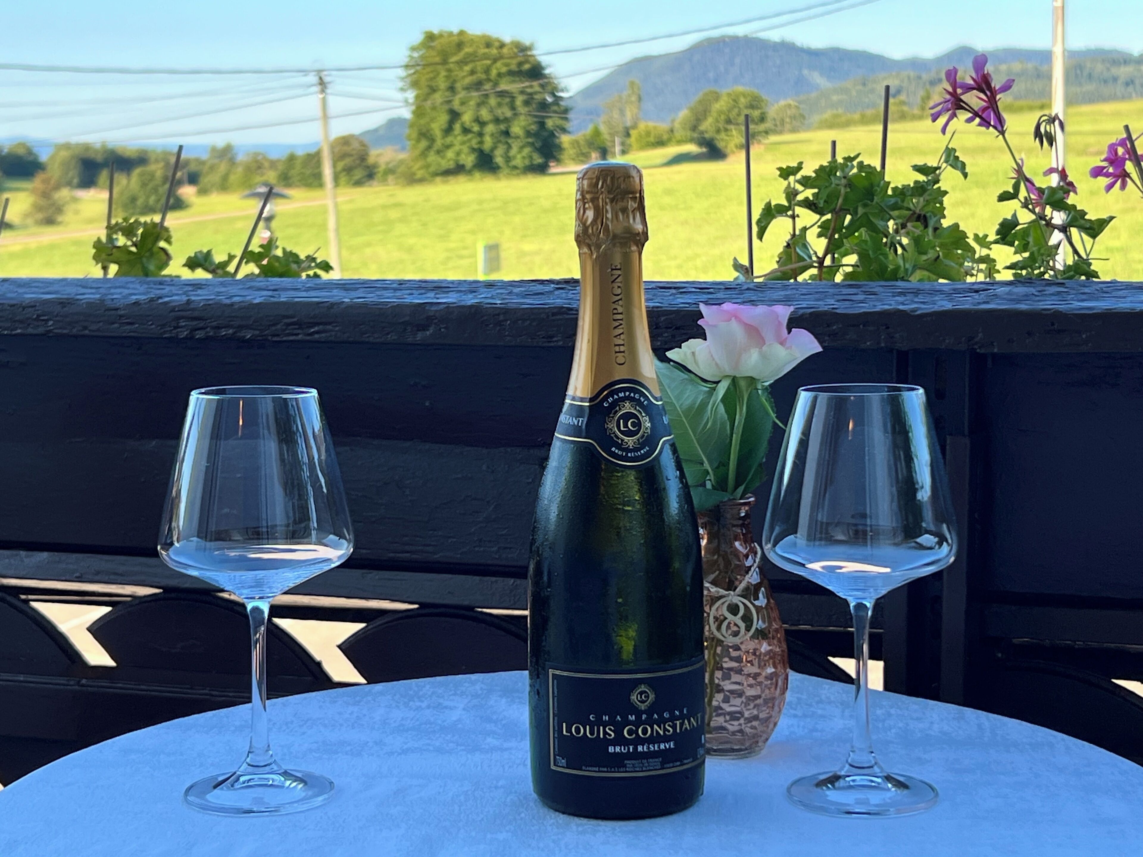 A bottle of Louis Constant Brut Reserve champagne on a table with two empty wine glasses.