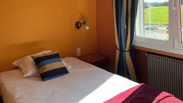Une chambre à coucher avec un lit, une table de chevet, une lampe fixée au mur et une fenêtre avec des rideaux.