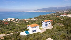 A coastal residential area with houses, a clear view of the sea, and a mountainous backdrop. - Modern Seaview Nest With Pool Panoramic Views (Kalamata)