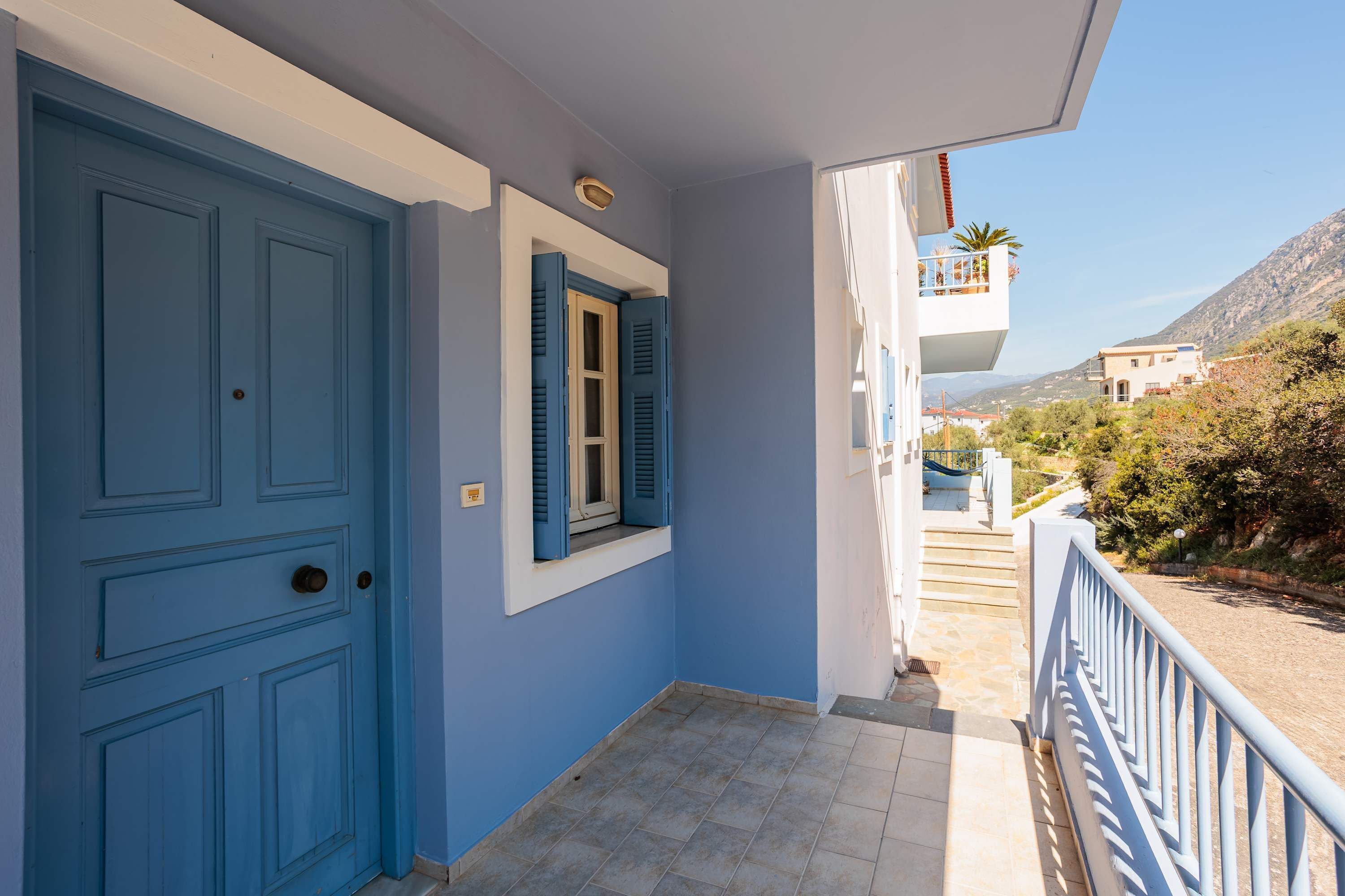 A blue door with shutters, a window with shutters, and a balcony with a railing.