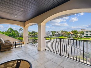 A covered balcony with a view of a residential area, a seating area with a table and chairs, and a railing. - Destiny's Paradise | Lux Home, Golf Cart, Private Pool (Destin)