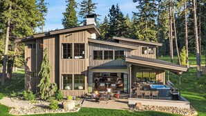 A modern two-story house with a large deck area, outdoor seating, and a hot tub.