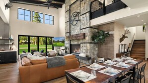A spacious living area with a fireplace, a dining table set for six, and a large window overlooking a golf course.