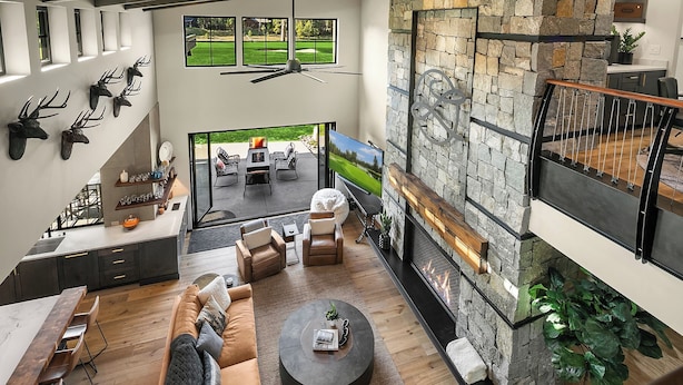 A spacious living area with a stone fireplace, a dining area with a long table, and a view of a golf course through large windows.