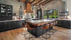 A modern kitchen with a large island, dark cabinetry, and a view of a garden.