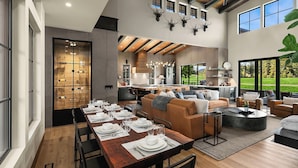 A spacious living area with a dining table set for four, a cozy seating area with a sofa and armchairs, and a kitchen in the background.