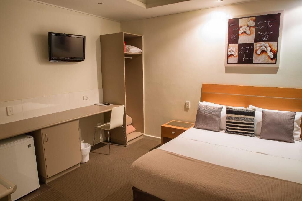A hotel room with a bed, a desk, a chair, a TV, and a wardrobe.