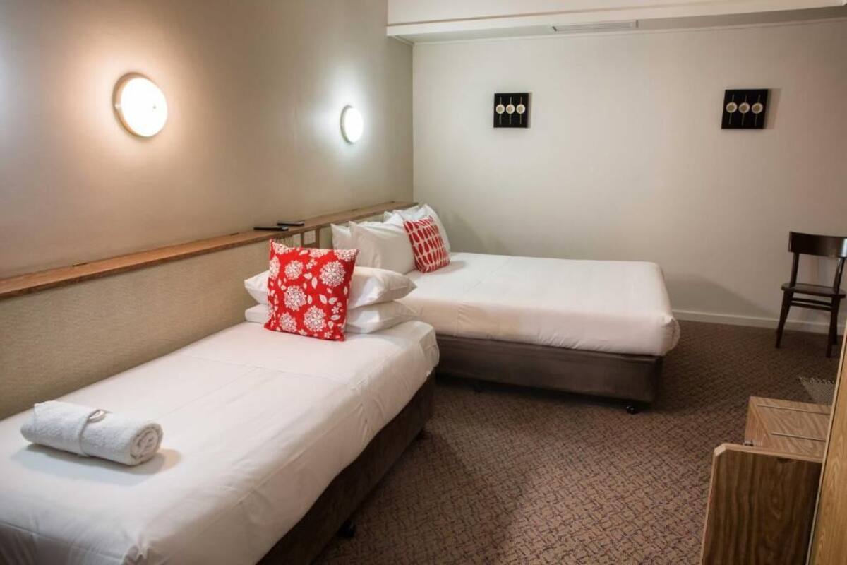 A hotel room with two single beds, a wooden headboard, a small desk, and a chair.