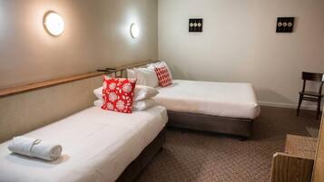 A hotel room with two single beds, a wooden headboard, a small desk, and a chair.