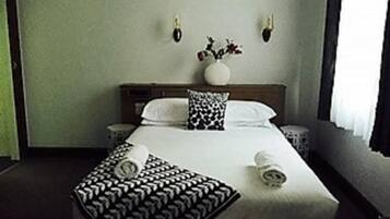 Une chambre d’hôtel avec un grand lit, deux tables de chevet, un vase avec des fleurs posé sur la tête de lit et une fenêtre avec des rideaux.