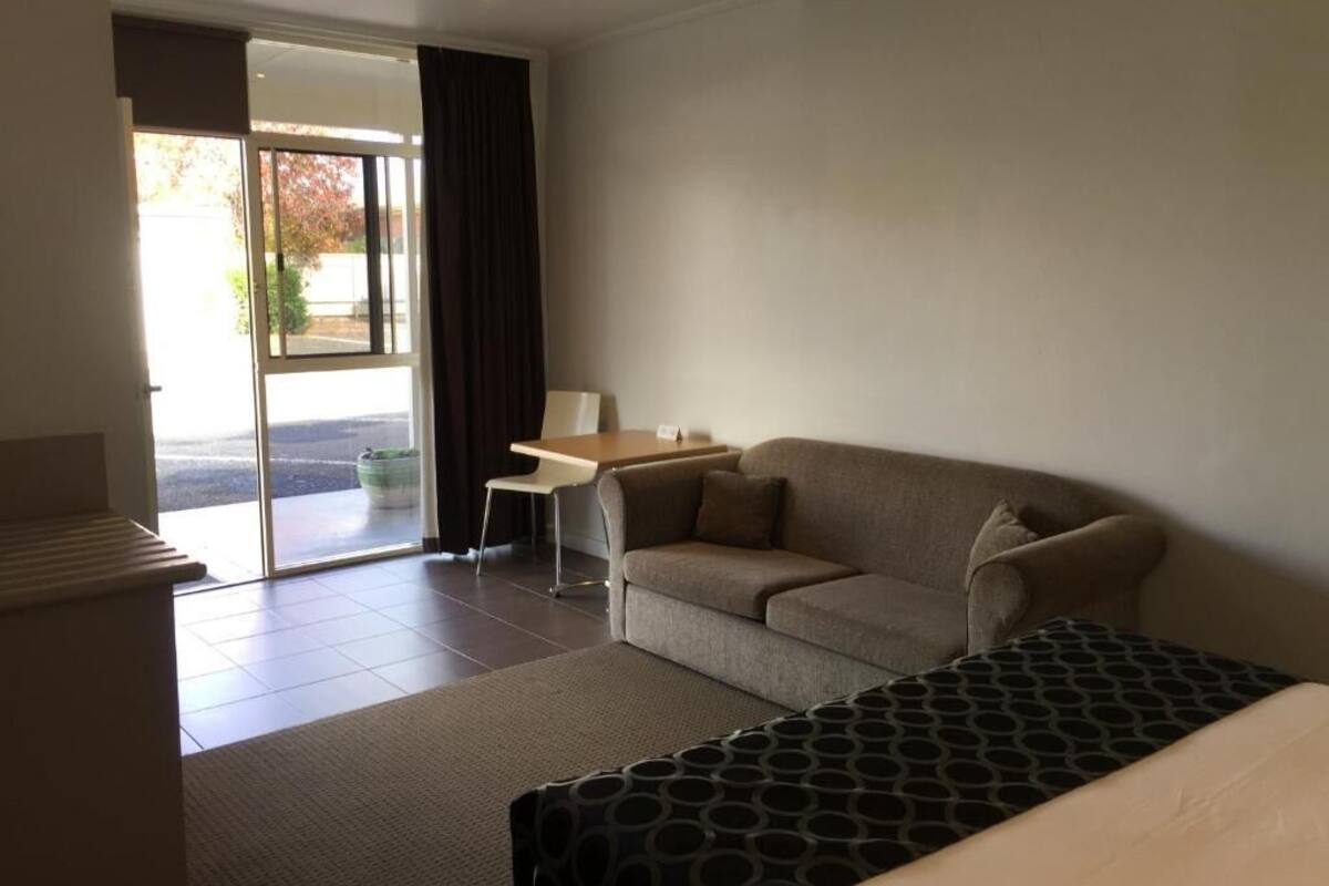 A hotel room with a sofa, a small table, and a patterned bedspread.