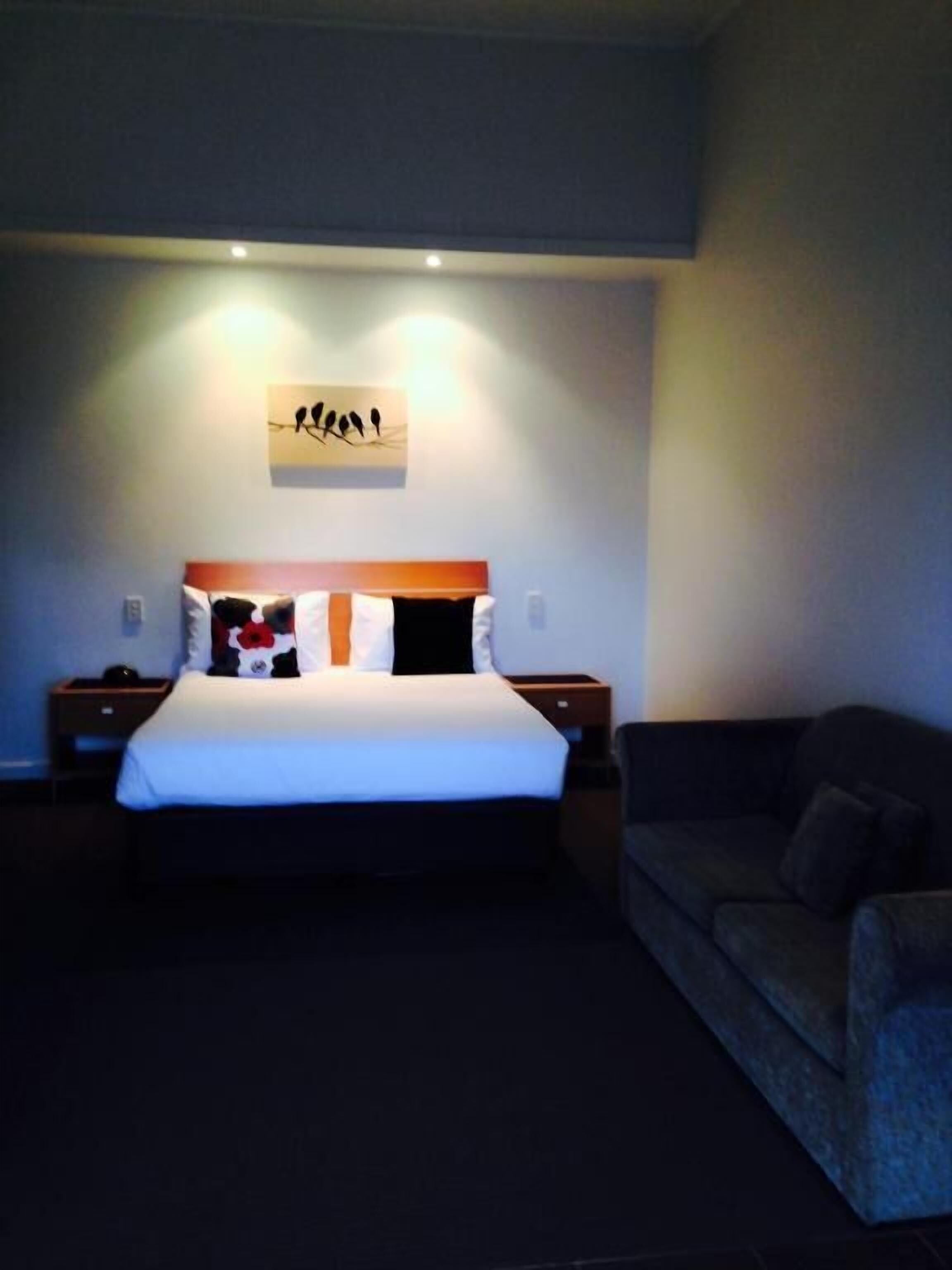 A bedroom with a large bed, a nightstand, a bedside table, and a couch.