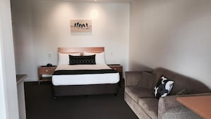 Un dormitorio con cama, mesita de noche, sofá y una obra de arte colgada en la pared.