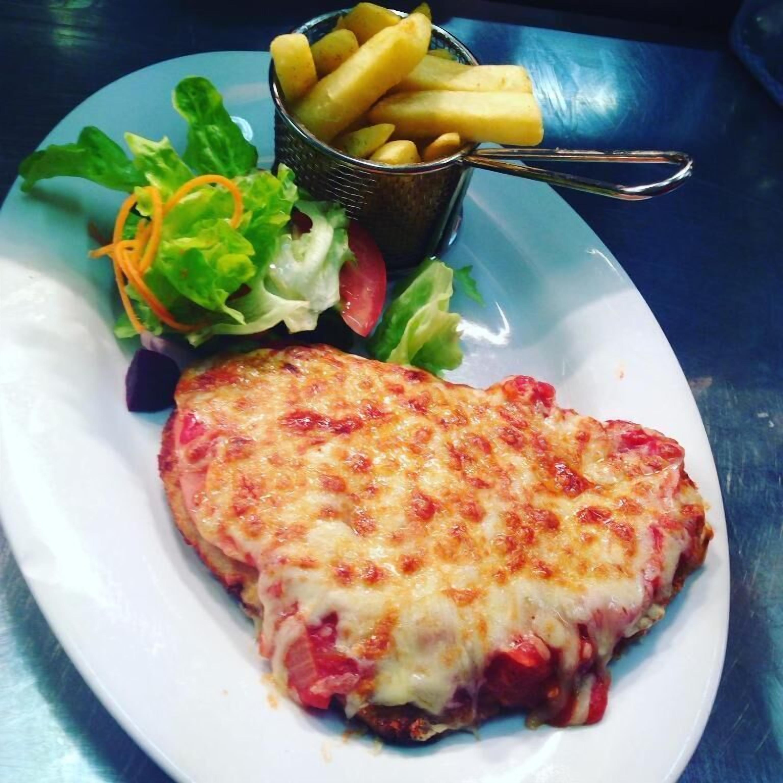 Ein Teller mit einem Hähnchenschnitzel, überbacken mit Käse, dazu ein gemischter Salat und eine kleine Portion Pommes.