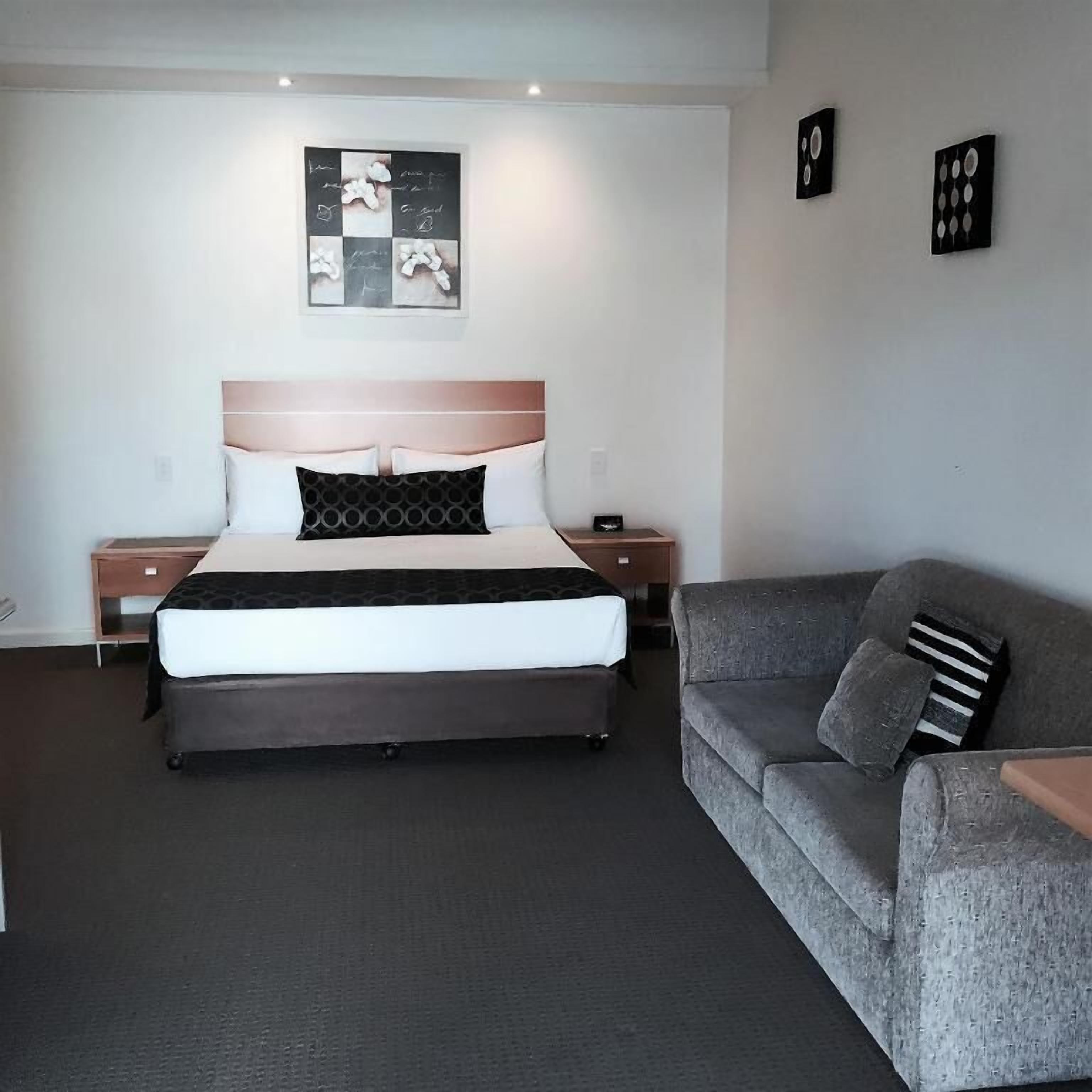 A hotel room with a bed, a gray sofa, and a wall-mounted artwork.