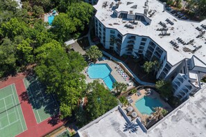 Vue aérienne d’un hôtel doté de plusieurs piscines, de courts de tennis et d’un espace sur le toit aménagé avec des chaises longues.
