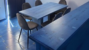 A room with a long table, six chairs, a door with a window, and a ceiling with exposed beams. - LINA'S HOUSE (Mykonos)